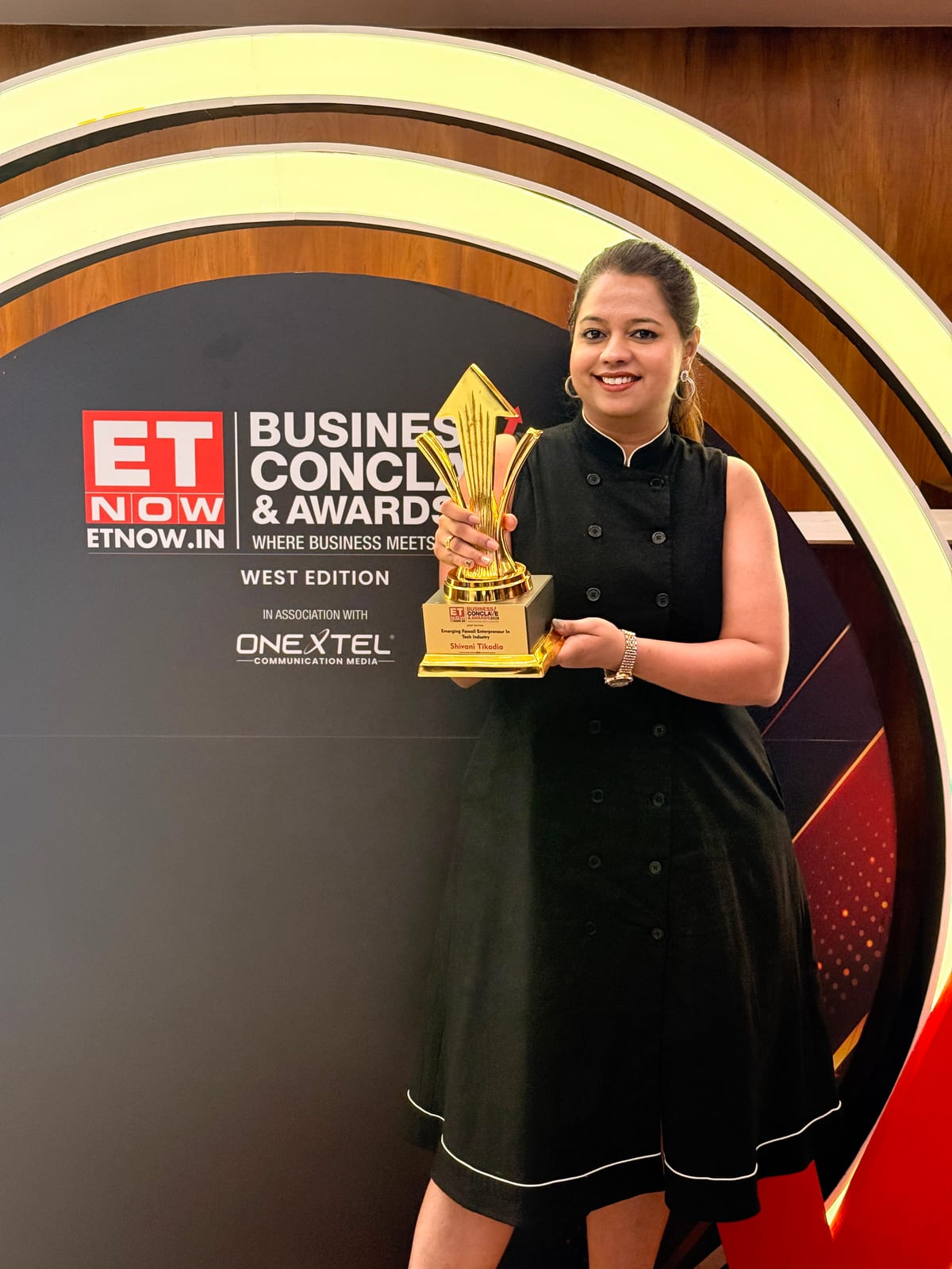 Shivani Tikadia holding the Emerging Female Entrepreneur in Tech Industry trophy in front of the ETNOW.in Business Conclave and Awards 2026 arch