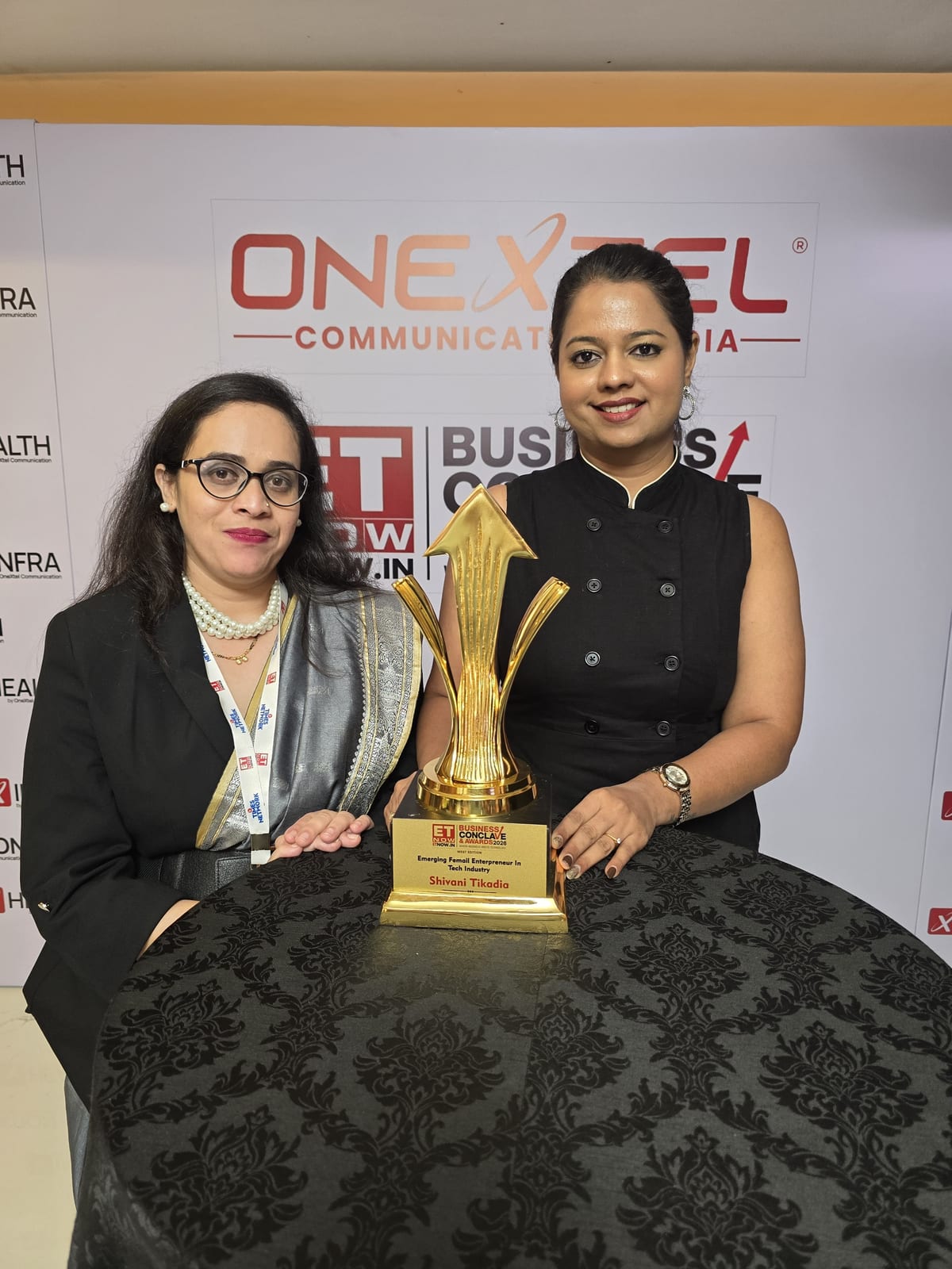 Shivani Tikadia with a SecComply colleague and a trophy in front of the ETNOW.in Business Conclave and Awards 2026 media wall